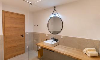 A modern bathroom with a large mirror and a wooden countertop. Towels are neatly arranged on the shelf.