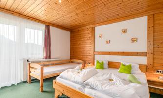 A cozy bedroom with wood paneling and two beds. There are large windows with curtains and some decorative pictures on the wall.