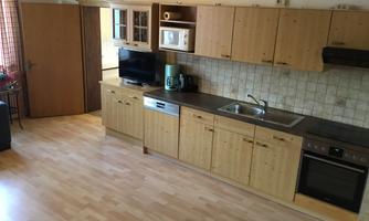 A modern kitchen with wooden cabinets and a countertop. It is equipped with a stove, a sink, and household appliances.