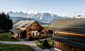 A picturesque mountain landscape with wooden chalets and high mountains in the background. The scene exudes tranquility and a connection to nature.