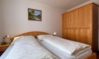 A cozy bedroom with a double bed and wooden wardrobes. On the wall hangs a painting of a landscape.