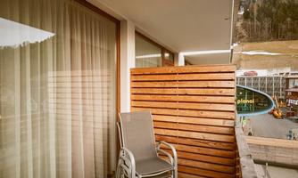 A balcony with wooden paneling and a seating chair. In the background, a mountain landscape can be seen.