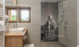 A modern bathroom with a clear glass shower wall. In the background, there is a large picture of two sheep.