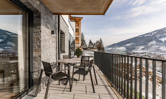 A modern balcony with a table and chairs. In the background, there are snow-covered mountains and a clear sky.