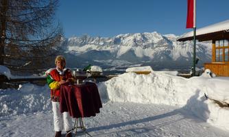 A woman stands in the snow with a table in the Alps. In the background, majestic mountains and a clear blue sky can be seen.