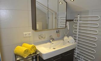 A modern bathroom with a sink and a large mirror. Yellow towels are neatly arranged and a towel rack is mounted on the wall.