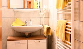 A modern bathroom with a white sink and wooden shelf. Yellow towels hang on a towel radiator.