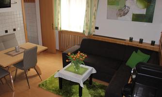 A cozy living area with a black sofa, a table, and chairs. A flower arrangement on a small table adds color to the room.