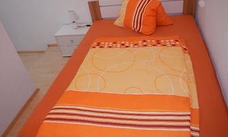 A simple bedroom with a single bed in warm shades of orange. Next to the bed, there is a nightstand with a lamp.
