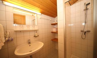 A bright bathroom with white tiles and wooden details. There is a sink, a shower, and mirror lighting.