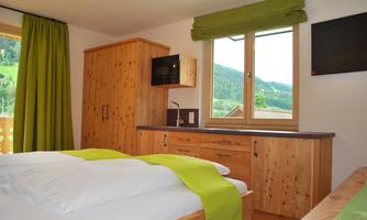 A cozy bedroom with wooden paneling and large windows. There are two beds, matching curtains, and a television on the wall.