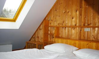 A cozy bedroom with a wooden wall panel and a skylight. The bed is decorated with white pillows and bed linen.
