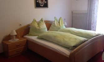 A cozy bedroom with a large bed and soft pillows. There is a bedside table and a window with curtains.