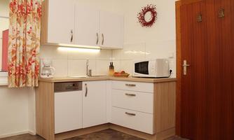 A modern kitchen with white cabinets and a gray floor. The space is bright and well-equipped with a microwave and other appliances.
