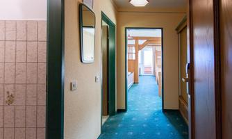 A bright hallway with green carpet and walls in neutral colors. At the end of the hallway, additional rooms are visible.