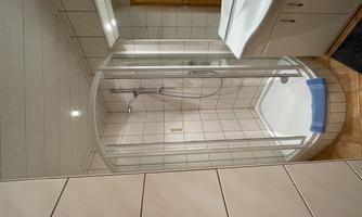 A modern bathroom with a shower cabin and a sink. The walls are tiled and the furnishings are bright and inviting.