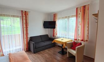 A bright living room with a cozy sofa and a table. Large windows let in a lot of daylight.