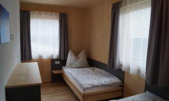 A simple room with two single beds and wooden paneling. Large windows let in plenty of light and create a cozy atmosphere.