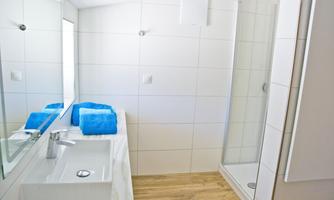 A modern bathroom with a sink, a large mirror, and a shower. The walls are tiled in light colors, and blue towels are placed on the table.