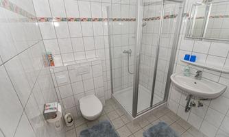 A modern bathroom with tiles, a shower, and a sink. There is a toilet and towels on the floor.