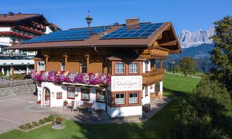A picturesque building in alpine style with solar panels and colorful flower boxes. In the background, the majestic mountains can be seen.