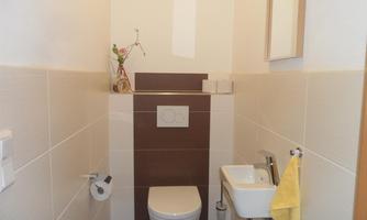 A modern bathroom with a toilet and a small sink. The walls are painted in neutral colors and there is a nice decoration.