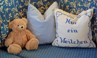 A cozy sofa with a fluffy bear and a decorative cushion. The cushion has the print "Just a little while."