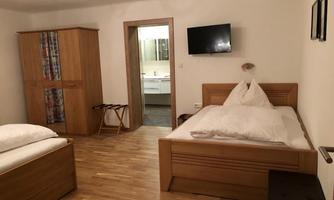 A simple bedroom with two beds and a wooden wardrobe. A television is mounted on the wall and a door leads to the bathroom.