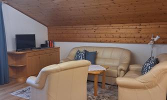A cozy living room with beige leather furniture and a wooden ceiling. There is a small table and a television in the corner.