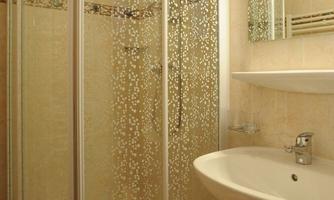 A modern bathroom with a glass shower cabin and a sink. Towels in soft colors are placed on a small stool.