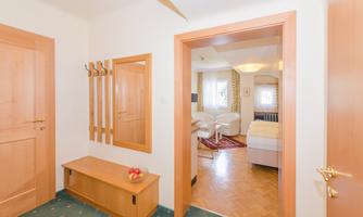 A bright hallway with wooden doors and a wardrobe. In the background, you can see a living area with modern furniture.