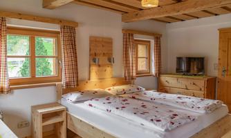 A cozy bedroom with a double bed and wood-paneled walls. The windows let in plenty of daylight and create an inviting atmosphere.