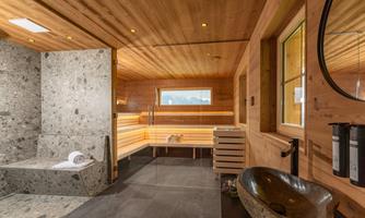 A modern sauna interior with wooden paneling and a stone washbasin. The room design creates a relaxing atmosphere with a window for daylight.