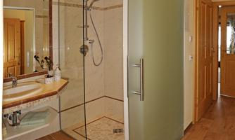 A modern bathroom with a shower and a sink. The floor is made of wood, and the walls are tiled.
