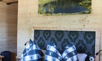 A cozy bedroom with wooden paneling and a large picture of a lake and mountains. The bedding has an appealing checked design with stylized animals.