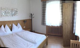 A cozy room with a double bed and a bunk bed. The room has windows with curtains and a modern TV system.