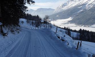 A snow-covered street, surrounded by trees and mountains. The landscape extends quietly in the background.
