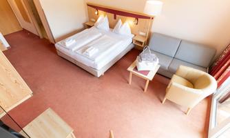 A cozy hotel room with a double bed, a sofa, and a table. The decor is bright and friendly, ideal for a relaxing stay.