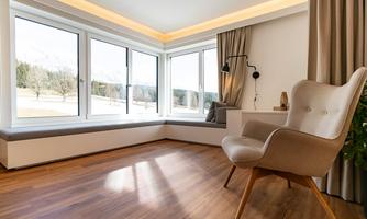 A bright room with large windows and a view of nature. A comfortable armchair stands in the corner on a wooden floor.