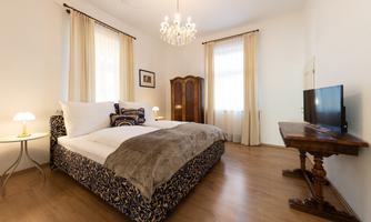 A cozy bedroom with a large bed and elegant decor. The room is bright and inviting, with a TV and a beautiful chandelier.