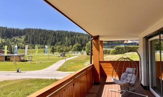 A cozy terrace with a hanging chair and a view of a green landscape. In the background, forests and a clear sky can be seen.