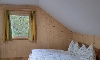 A cozy bedroom with a double bed and bright pillows. Large windows let in plenty of daylight and offer a view of nature.
