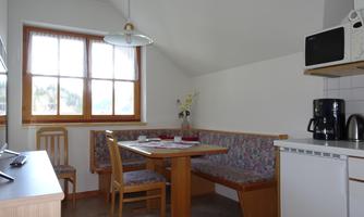 A cozy dining area with a corner table group and bright windows. In the corner, there is a microwave and a coffee machine.