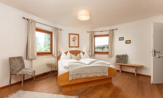 A cozy bedroom with a double bed and wooden floor. Large windows let in plenty of light and create an inviting atmosphere.