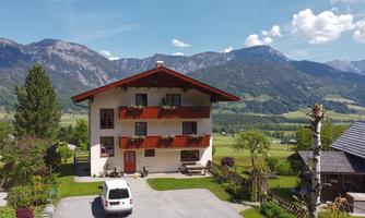 A charming house in the Alps with colorful flower boxes and a clear blue sky. In the background, majestic mountains and green meadows stretch out.