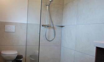 A modern bathroom with a glass shower and cozy design. The walls are light and the floor tiles are dark.