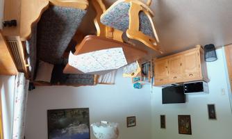 A cozy dining area with a large table and wooden benches. In the background, there is a television and a sideboard.