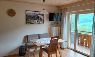 A cozy dining area with a table and two chairs. A television and large windows provide a view outside.