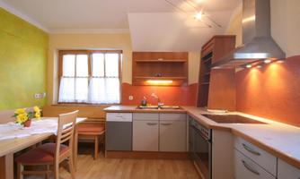 A modern kitchen with a wooden floor and bright walls. Fresh flowers are on the table and the countertop is tidy.