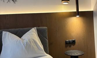 A cozy bedroom with a modern bed and elegant lighting elements. A stylish tree design can be seen on the wall.